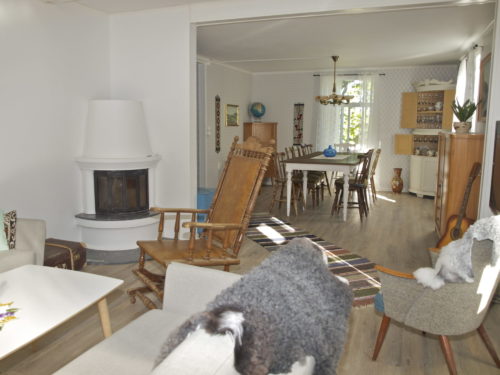 Ferienhaus, Austrått Agrotourismus, Kårstua, wohnzimmer, weißer kamin rechts, Stühle mit schaffell, esstisch im hintergrund
