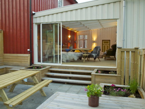 Austrått agrotourismus, Kårstua, wintergarten mit glasschiebetüren, esstisch drinnen und draußen mit Bänken, schafspelz auf Stuhl und bänken im wintergarten
